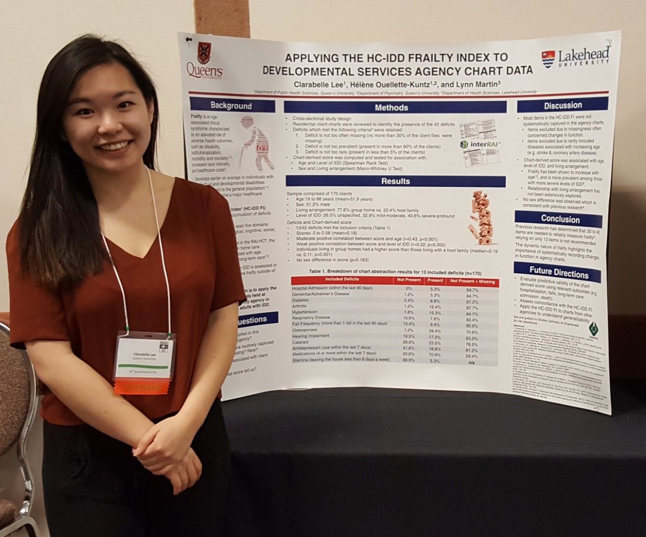 A young woman professional dressed stands smiling next to her poster on the frailty index.